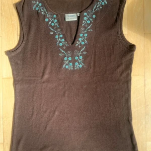 Brun ärmlös topp med broderi - Brun ärmlös topp med v-ringning och detaljerat turkost blommigt broderi längs halsringningen🥰