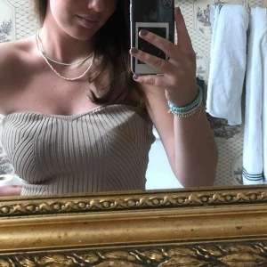 Beige ribbad tubtopp - Säljer en beige ribbad tubtopp med bandeau-modell. Toppen är figurnära och stickad