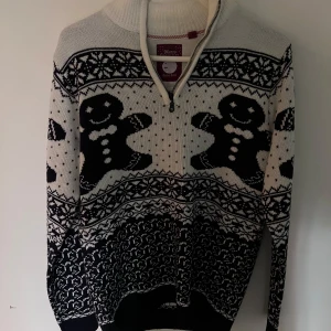 Jultröja Brave Soul med pepparkaksgubbar - Säljer en svartvit jultröja från Brave Soul med pepparkaksgubbar och snöflingor som mönster. Tröjan har hög krage och half zip-dragkedja framtill. Stickad i mjukt material och har långa ärmar. Perfekt för dig som vill sticka ut på julmiddagen!