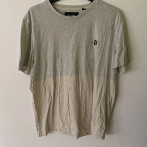 Ljusgrå och beige t-shirt Lyle & Scott - T-shirt från Lyle & Scott i storlek XXL. Tvåfärgad design med ljusgrå överdel och beige nedtill. Klassisk rund hals och korta ärmar. På bröstet sitter den ikoniska broderade gula örnen. Skön och lätt i bomull.
