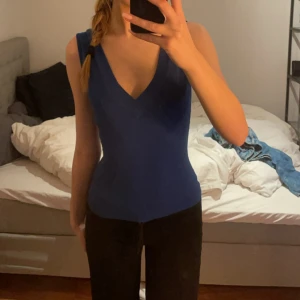 Blå ribbad v-ringad linnetopp - Säljer en snygg blå ribbad linnetopp med djup v-ringning både fram och bak. Toppen är ärmlös och har en tight passform som framhäver figuren. Perfekt att styla med jeans eller kjol för en clean look.