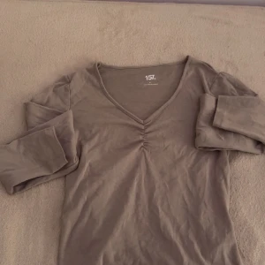 Beige långärmad tröja från 157 - En stilren beige långärmad topp från 157 med v-ringning och snygg rynkdetalj framtill. Toppen är i mjuk bomull och har en enkel, croppad passform som passar perfekt till jeans eller kjol.