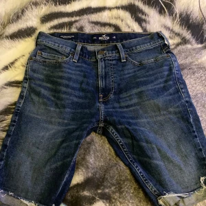  jeansshorts från Hollister - Mörkblå jeansshorts från Hollister med råa kanter nertill. Klassisk femficksmodell i stretchigt denim med snygga slitningar och orange kontrastsömmar. Perfekta för dig som gillar en tight passform och stilren look. För endast 200kr kan förhandlas vid snabb affär👌☺️
