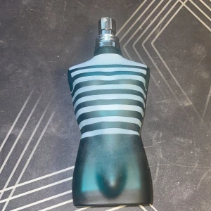Jean Paul Gaultier la male - Säljer en unik parfymflaska formad som en manlig torso med blå och turkosa ränder. Flaskan har en stilren design med en metallisk spraytopp. Perfekt för den som vill ha en iögonfallande detalj på hyllan.