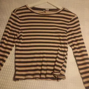 Säljer en randig långärmad tröja från H&M i beige, svart och brun. Tröjan har en ribbad struktur och en normal passform. Perfekt för höst och vår!