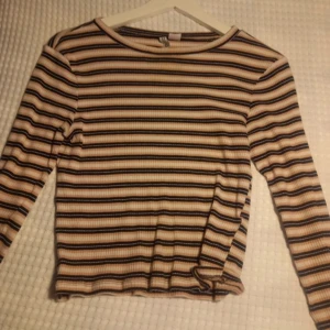 Randig långärmad tröja från H&M - Säljer en randig långärmad tröja från H&M i beige, svart och brun. Tröjan har en ribbad struktur och en normal passform. Perfekt för höst och vår!
