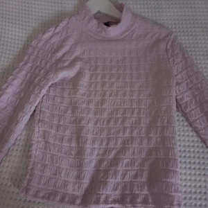 Ljuslila ribbad tröja - Säljer en söt ljuslila tröja med ribbad struktur. Tröjan har långa ärmar och en hög krage som ger en stilren look. Perfekt för kyligare dagar.