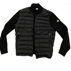 Svart Moncler cardigan - Moncler cardigan i storlek Small.  Jackan är i mycket bra skick då den knappt kommit till användning. Osäker på autenticitet då den köptes begagnad. Kontakta för exakta mått fler bilder eller funderingar😇