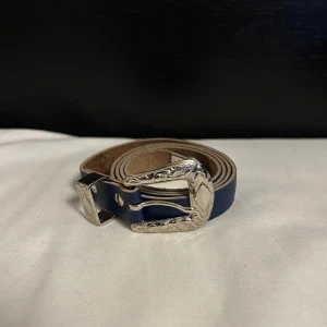 Blått bälte med silverdetaljer - Snyggt blått bälte med dekorativt silverspänne. Perfekt för att ge en extra touch till din outfit. Inga tecken på användning 