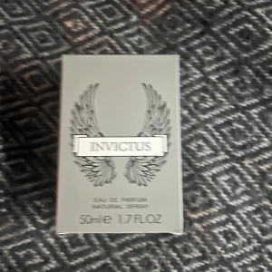 Invictus Eau de Parfum 50ml - Säljer en flaska Invictus Eau de Parfum, 50 ml. Flaskan har en unik design som liknar en trofé, med silverdetaljer och en elegant form. Perfekt för den som vill ha en fräsch och maskulin doft.