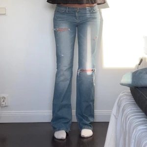 Lågmidjade utsvängda jeans - Snygga blå utsvängda jeans med slitningar på knäna. De har en klassisk femficksdesign och en låg midja. Perfekta för en avslappnad stil. Midjemåttet är ca 86 cm, innerbenslängden är ca 87 cm och grenmåttet är ca 21 cm. Storlek W30 L36, jag är ca 177 cm. Märket är Topshop Tall. Liten fläck på benet, går säkert bort i tvätten. Samt slitningar och hål längst ner på byxorna. Defekterna syns på de sista bilderna. 