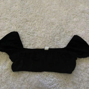 Svart kort topp från Divided - Snygg svart topp från Divided. Perfekt för en stilren look med sina korta ärmar och elastiska detaljer. Passar utmärkt till både jeans och kjol. Passar även som topp på stranden! Står Storlek M, men skulle säga att de är en S
