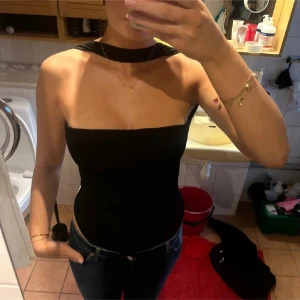 Svart axelbandslös topp - Snygg svart axelbandslös topp med hög hals och öppen rygg. Perfekt för en kväll ute eller en speciell tillställning. Toppen har en tight passform som framhäver figuren. (lånade bilder)
