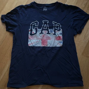 Mörkblå t-shirt från GAP - Säljer en mörkblå t-shirt från GAP med ett stort tryck av Union Jack-flaggan och GAP-loggan på framsidan. Köpt på GAP-store i London.
