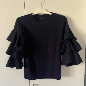 Tröja  - Snygg marinblå tröja från Votelle med unika volangärmar som ger en trendig look. Perfekt för att piffa upp din garderob med något speciellt. Passar bra till både jeans och kjol.