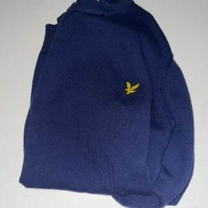 Mörkblå tröja från Lyle & Scott - Säljer en stilren mörkblå tröja från Lyle & Scott med deras ikoniska gula logga på bröstet. Tröjan har långa ärmar och en klassisk rund halsringning. Perfekt för en avslappnad men ändå snygg look.