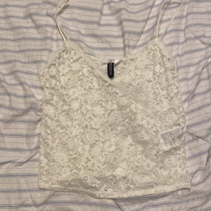 Vit spetslinne  - Säljer ett sött vitt spetslinne. Linnet har tunna axelband och ett vackert blommigt spetsmönster. Perfekt för varma sommardagar eller som ett lager under en kavaj. Aldrig använt 