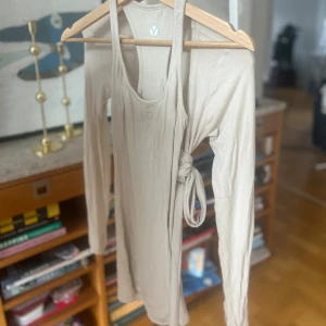 Beige set för pilates/yoga - Säljer en beige onesie och omlottkofta från Evenwood Active. Toppen är ärmlös och har en stilren design med rund halsringning. Supermjuk modal och stretchigt tyg.