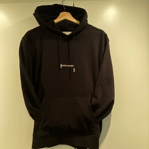 Svart hoodie från Saint Laurent - Snygg svart hoodie från Saint Laurent med en minimalistisk logga på bröstet. Den har en klassisk design med justerbar huva och en stor magficka. Perfekt för en stilren och bekväm look. 10/10 Skick! 🍻