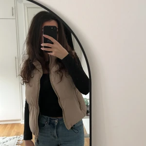 Beige dunväst från FB Sister (NEWYOURKER - Säljer en snygg beige dunväst från FB Sister. Västen har en dragkedja framtill och är perfekt för lager-på-lager under kyligare vårdagar. Den är stilren och lätt att matcha med olika outfits. Storleken är S men den funkar som XS också, västen är endast använd 3 gånger. Pris kan diskuteras 