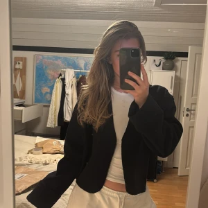 MÖRKBLÅ kavaj/jacka tunn GinaTricot - Säljer en stilren svart  med knappar framtill. Kavajen har en croppad design och långa ärmar, perfekt för en trendig look. Passar bra till både vardag och fest. Endast använd 1 gång, ser svart ut men är mörkblå! 