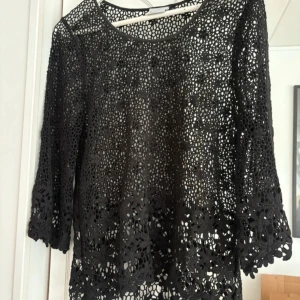 Svart spetsblus från Jeena - Säljer en elegant svart spetsblus från Jeena med vackert blommönster. Blusen har trekvartsärmar och en luftig design som passar perfekt för både vardag och fest. Perfekt för att lägga till en touch av stil till din garderob!