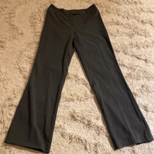 Grå/svart  kostymbyxor från KappAhl - Snygga grå/svarta kostymbyxor från KappAhl med en klassisk design. Byxorna har en rak passform och stängs med två knappar i midjan. Perfekta för en stilren look.