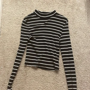 Svart och vit randig tröja från H&M Divided - Säljer en svart och vit randig tröja från H&M Divided. Tröjan har långa ärmar och en hög krage, perfekt för en stilren look. Passar bra till både jeans och kjol. Hör av dig vid intresse!