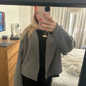 Grå kappa - Säljer en stilren grå kappa med en modern och minimalistisk design. Jackan har en lös passform och långa ärmar, perfekt för höst och vår. Den är tillverkad i ett mjukt material som ger en bekväm känsla.