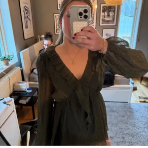 Olivgrön blus med volangdetaljer🫒🍸 - Snygg olivgrön blus med volangdetaljer och v-ringning. Blusen har långa ärmar och en luftig passform, perfekt för en stilren look.