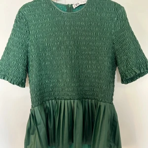 Grön topp från Zara - Snygg grön topp från Zara med smockdetaljer och korta ärmar. Toppen har en volangkant nedtill som ger en fin siluett. Perfekt för att piffa upp vardagslooken eller för en kväll ute.