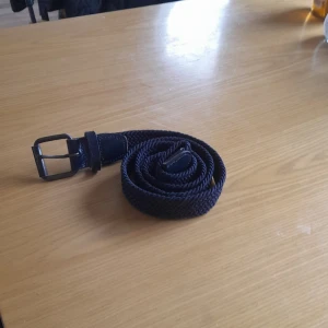 Blått flätat bälte - Snyggt blått flätat bälte med en klassisk metallspänne. Perfekt för att ge en stilren touch till din outfit. Bältet är flexibelt och passar till många olika stilar.