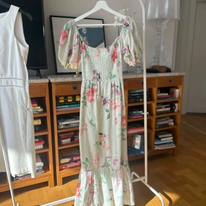 Blommig långklänning  - Superfin långklänning från ASOS med blommigt mönster i rosa och mint. Klänningen har korta puffärmar och en vacker öppen rygg med knytning. Perfekt för sommarens festligheter!
