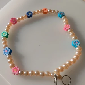 Pärlhalsband med färgglada blommor - Charmigt halsband med pärlor och färgglada blommor i olika nyanser. Perfekt för att lägga till en lekfull touch till din stil. Armbandet har en mix av rosa, blå, gröna och orange blommor som ger en härlig färgklick. Pris kan sänkas! 