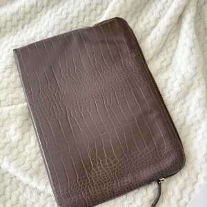 Brun/lila datorväska i skinn med croco-mönster - Säljer en stilren brun datorväska i skinn med croco-mönster på ena sidan och slät baksida.  35x25 cm 🤍