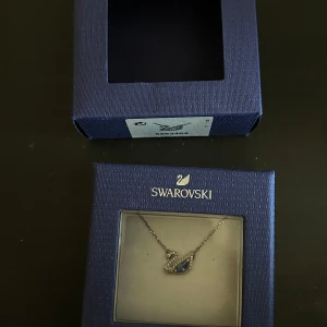 Swarovski halsband  - Ett elegant halsband från Swarovski. Smycket har en vacker svan design.  Ett silvrigt halsband från Swarovski med blå Sten i mitten av svanen. Inköpt för 1000kr helt nytt  Halsbandet är endast testat och har därför inga defekter