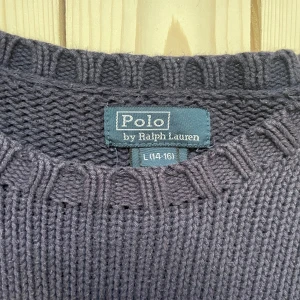 Mörkblå stickad tröja Polo Ralph Lauren - Säljer en mörkblå stickad tröja från Polo Ralph Lauren med amerikansk flagga och RL-broderi på bröstet. Tröjan har rund hals, ribbade muddar och är långärmad. Perfekt för dig som gillar att ha klass. Storlek L 14/16