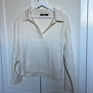 Ribbad krämvit tröja från BikBok - Superfin ribbad tröja från BikBok i krämvit färg. Tröjan har en snygg krage med v-ringning och långa ärmar. Den är stickad och har en relaxed fit som är perfekt till jeans eller kjol. Enkel men ändå stilren, passar perfekt till lager-på-lager.