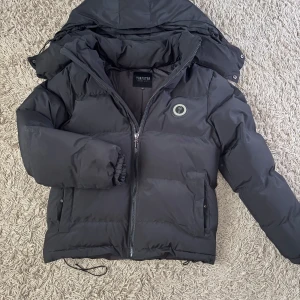 Svart pufferjacka från Trapstar XS - PRIS KAN DISKUTERAS GÅR INTE UNDER 1100!! Svart pufferjacka från Trapstar med broderad logga på ryggen och rund patch på bröstet. Jackan har huva som går att ta bort och sätta på igen, dragkedja framtill och elastiska muddar vid ärmslut. Perfekt för kalla dagar