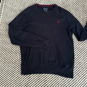 Mörkblå tröja från Polo Ralph Lauren - Snygg mörkblå tröja från Polo Ralph Lauren med klassisk röd logga broderad på bröstet. Tröjan är i 100% bomull, har rund hals och långa ärmar. Perfekt för dig som gillar stilren och tidlös design.