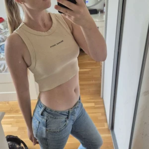 Beige topp från Abrand Jeans - Säljer en ribbad, croppad linnetopp från Abrand Jeans i beige. Toppen är ärmlös med breda axelband och har en tight passform. Materialet är mjuk bomull med stretch och logga broderad framtill. Perfekt till skolstarten! Säljer då den inte används, använd fåtal gånger. Hör gärna av dig vid frågor💕