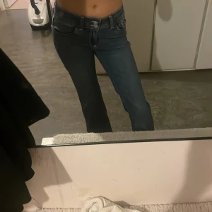 Blå bootcut jeans från Nelly - Snygga blå bootcut jeans från Nelly med låg midja och klassisk femficksmodell. Jeansen har vita kontrastsömmar och cool broderad detalj på bakfickorna. Tillverkade i mjukt denim med lätt stretch för skön passform.