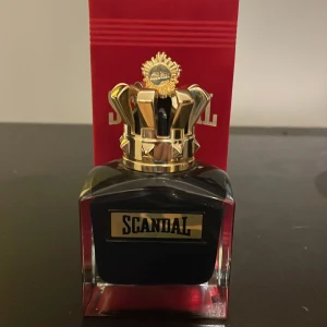 Scandal le parfum Jean Paul Gaultier 90/100 - Snygg parfymflaska från Jean Paul Gaultier, Scandal. Flaskan är svart med guldiga detaljer och en unik kronformad kork. Kommer i en röd förpackning med guldtext. Flaskan är fyrkantig och känns lyxig och tung i handen. Ungefär 90ml/100ml