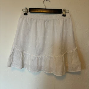 Broderad volangkjol  - Vit kjol med hålmönster/broderade blommor. Har en liten volangkant längst ner och resår i midjan. Står Hugh Waits på lappen men jag har haft den som en lågmidjad kjol. Volangen har låstnat lite på ett ställe (ner till höger på första bilden).  Midja: 35 cm mätt platt men kan bli större än så eftersom den har resår. Längd: 39/40 cm  Skriv om du har några frågor🩷