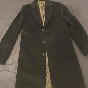 Svart kavaj med klassisk krage - Stilren svart rock med tre knappar framtill och klassisk krage. Jackan har raka fickor på sidorna och ett beige innerfoder som ger en snygg kontrast. Perfekt för dig som vill ha en tidlös och clean look under kallare dagar. Storlek=S