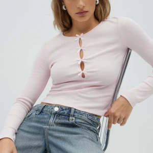 Ljusrosa långärmad topp med rosetter - Supersöt ljusrosa långärmad topp från Gina Tricot med croppad passform. Framsidan har flera små rosetter och öppna detaljer längs bröstet som ger en unik look. Tillverkad i mjuk ribbad bomullsmix som är skön mot huden.