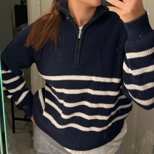 Marinblå randig stickad tröja half zip - Säljer en marinblå stickad tröja med vita ränder och half zip-dragkedja i halsen. Tröjan har ribbade muddar och lång ärm, perfekt för dig som gillar en avslappnad men ändå snygg stil. 