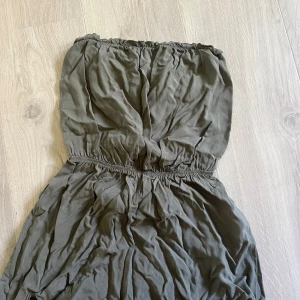 Olivgrön axelbandslös jumpsuit - Säljer en olivgrön axelbandslös jumpsuit med resår i midjan. Storlek 36, från h&m