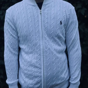 Vit kabelstickad kofta från Polo Ralph Lauren - Vit kabelstickad kofta från Polo Ralph Lauren med hel dragkedja framtill och klassisk svart logga på bröstet. Tröjan har ribbade muddar och krage, samt långärmad passform. Perfekt för dig som gillar stilren och tidlös design..          Nypris: 3145kr GORILLAPRIZE:1680kr             Skick:10/10 oöppnad          KVITTO MEDKOMMER 