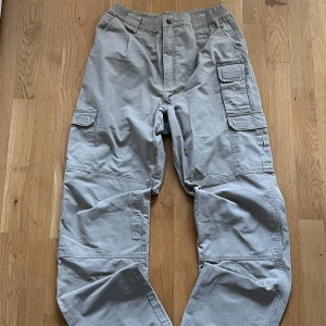 5.11 Tactical cargopants - Säljer ett par grå cargopants från 5.11 Tactical med flera praktiska fickor och elastisk midja. Byxorna har breda ben och är tillverkade i slitstark bomull, perfekta för dig som gillar funktionell och avslappnad stil. Snygga detaljer med förstärkningar och hällor. Mer information, bilder och prisdiskutering i dm. 